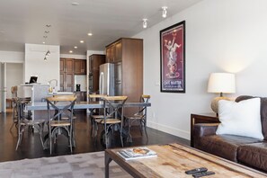 A modern living room with a brown leather sofa, a wooden coffee table, and a dining area with metal chairs and a wooden table. - Outpost: King Ridge 3 - AC & Hot Tub! (Jackson)