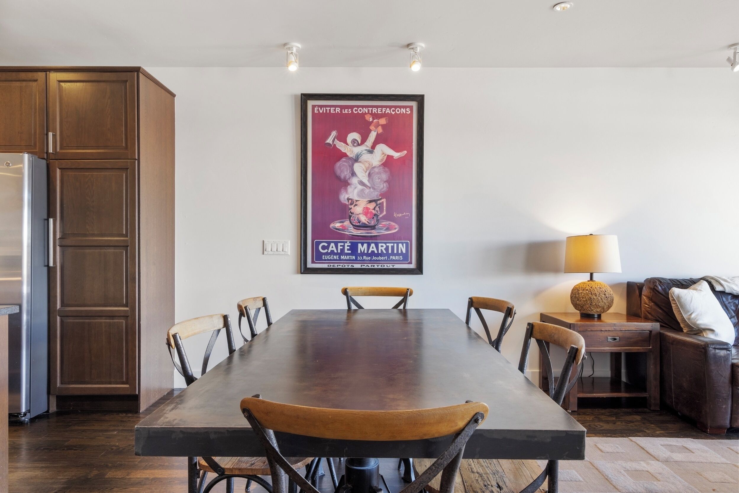 Un comedor con mesa de madera, sillas, un cartel y una lámpara.