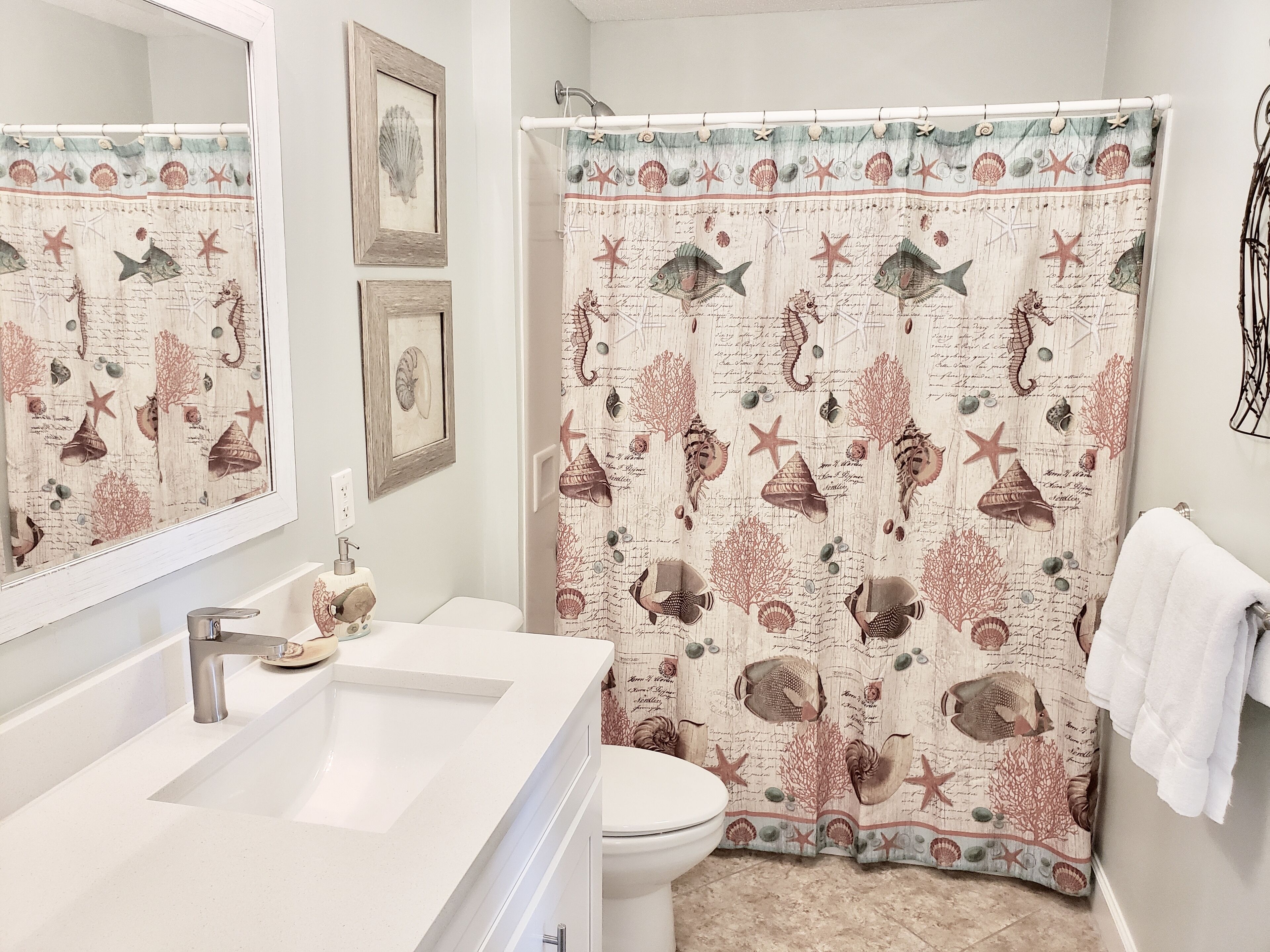 A bathroom with a white sink, toilet, and shower curtain with a marine theme.
