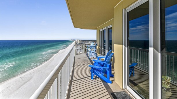 Un balcon avec vue sur la plage et l’océan, agrémenté de chaises bleues et d’un espace abrité.