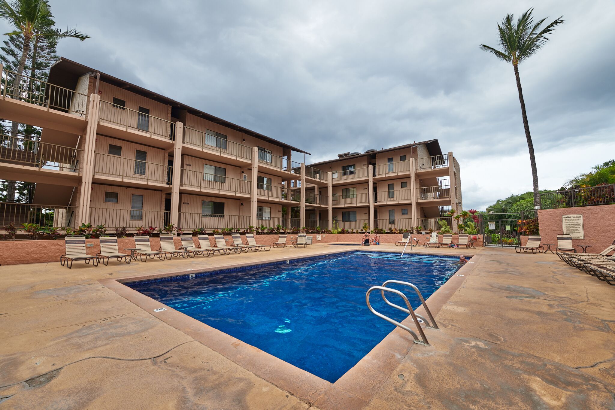 Un hôtel à plusieurs étages doté d’une piscine, d’un espace extérieur aménagé et de palmiers.