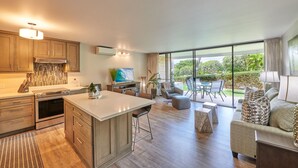 A modern kitchen with a central island, a dining area with a table and chairs, and a living room with a sofa and a TV.