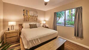 A bedroom with a bed, bedside lamps, a ceiling fan, a window with curtains, and a wall art piece.