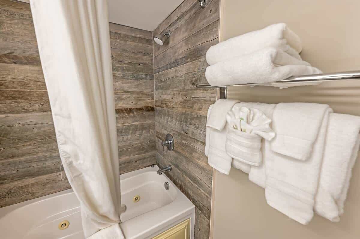 A bathroom with a wooden wall, a bathtub, and a towel rack with folded towels.