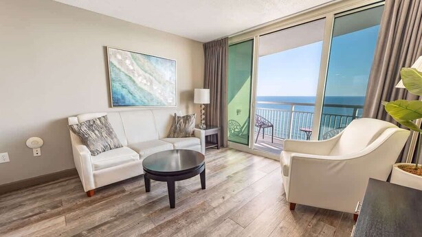 Een moderne hotelkamer met een ruim balkon, een witte bank, een ronde salontafel en uitzicht op de oceaan.