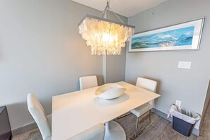 Ein Essbereich mit einem weißen Tisch, vier Stühlen, einer modernen Pendelleuchte und einem gerahmten Bild an der Wand.