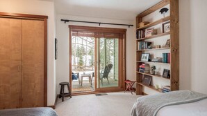 A bedroom with two beds, a wooden bookshelf, and a sliding glass door leading to an outdoor area with chairs and a table.