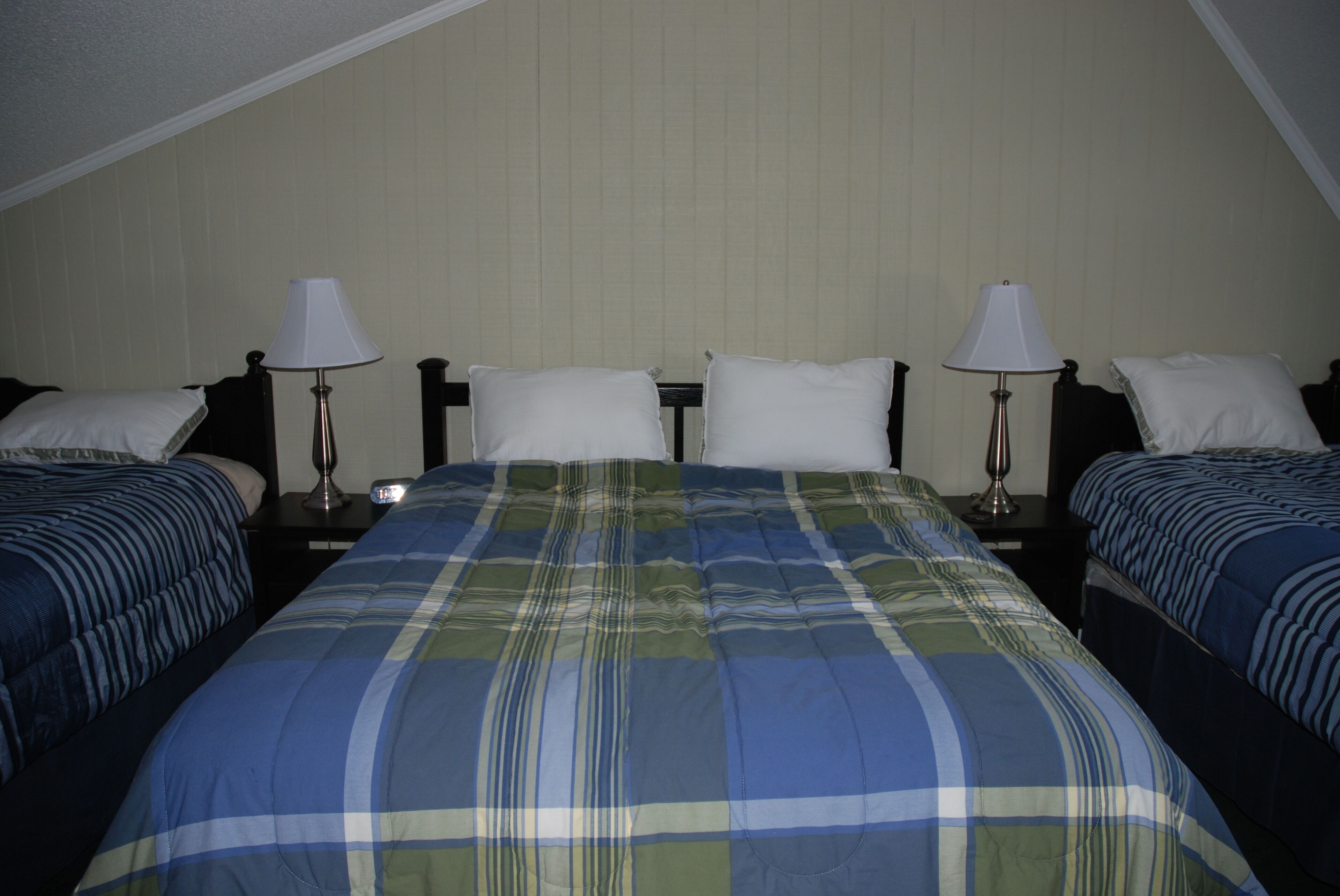 Habitación de hotel con dos camas individuales, una cama grande con cubrecama escocés y dos mesitas de noche con lámparas.