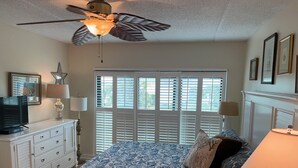 A bedroom with a bed, a ceiling fan, a dresser, a television, and a window with blinds. - MARLIN QUAY,  2 BR , 2  bath , Unit 205, ELEVATOR,  Pools, overlooks Marina<br> (Murrells Inlet)