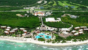 An aerial view of a resort with a central building, multiple guest villas, a beach, and a large pool.
