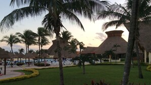 A resort with thatched-roof buildings, palm trees, and a pool area.