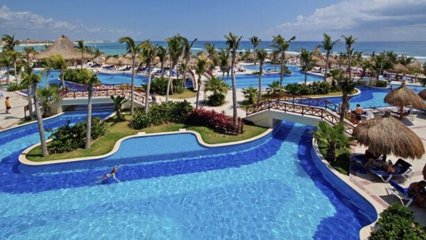A resort with multiple swimming pools, palm trees, and a beach view.