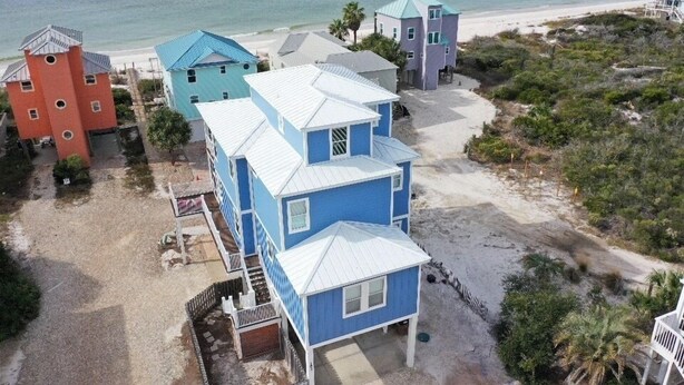 Um imóvel à beira-mar com vários edifícios, incluindo uma casa azul destacada com telhado branco e uma estrutura vermelha em formato de torre.