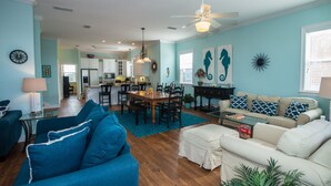 Uma sala de estar ampla com um sofá azul, um sofá branco e uma área de jantar com mesa e cadeiras de madeira.