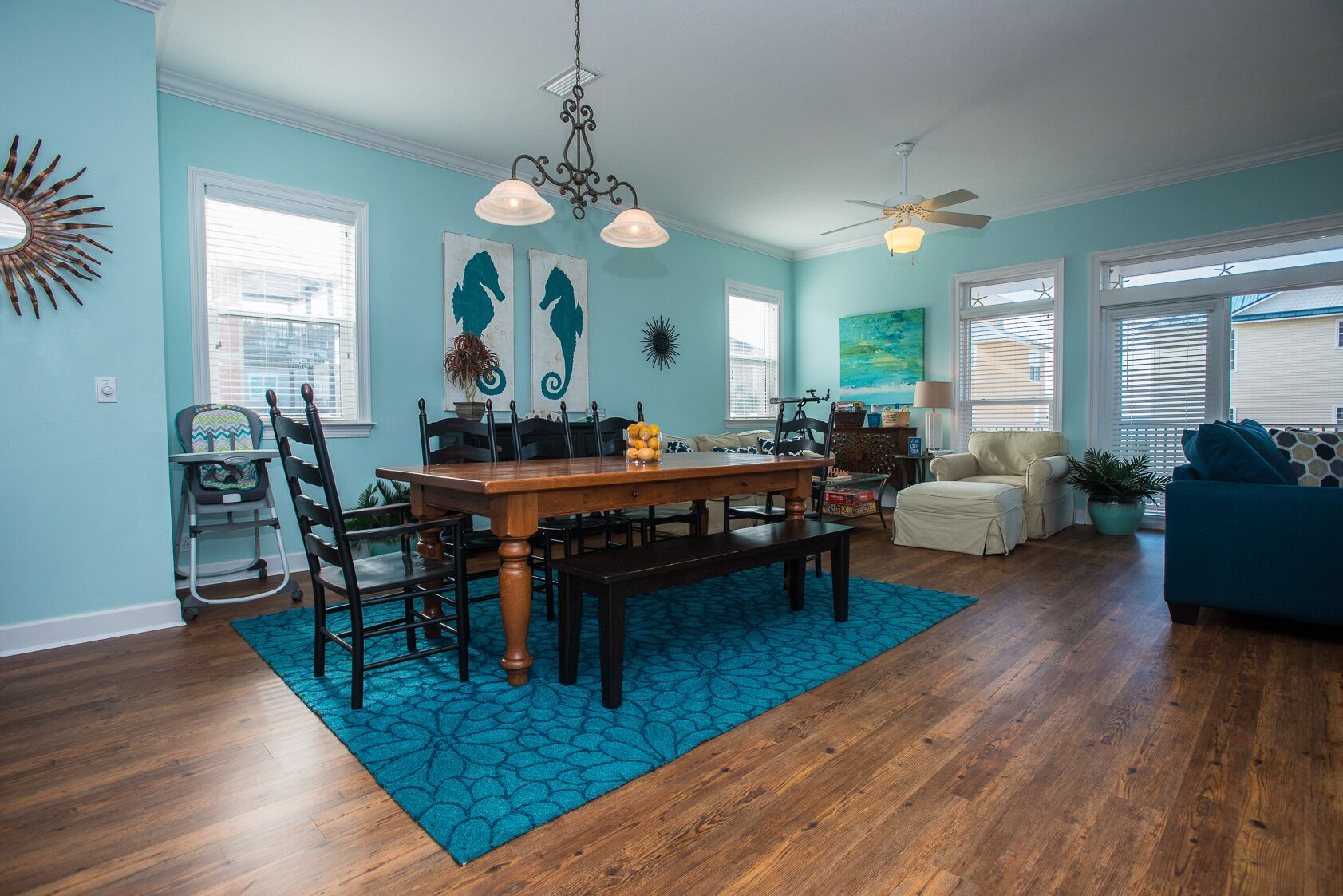 A dining area with a wooden table and chairs, a blue patterned rug, and a ceiling fan.