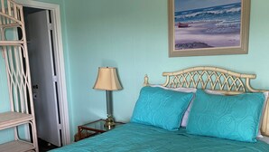 A bedroom with a bed, a nightstand, a lamp, a chair, and a door. - APATBIII Ocean Side/Ocean View 9520 SHORE DR 3P Family friendly.  (Myrtle Beach)
