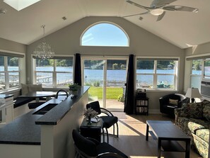 Una cocina amplia con una isla grande, un comedor con sillas, un sofá y vistas a un lago a través de amplios ventanales.