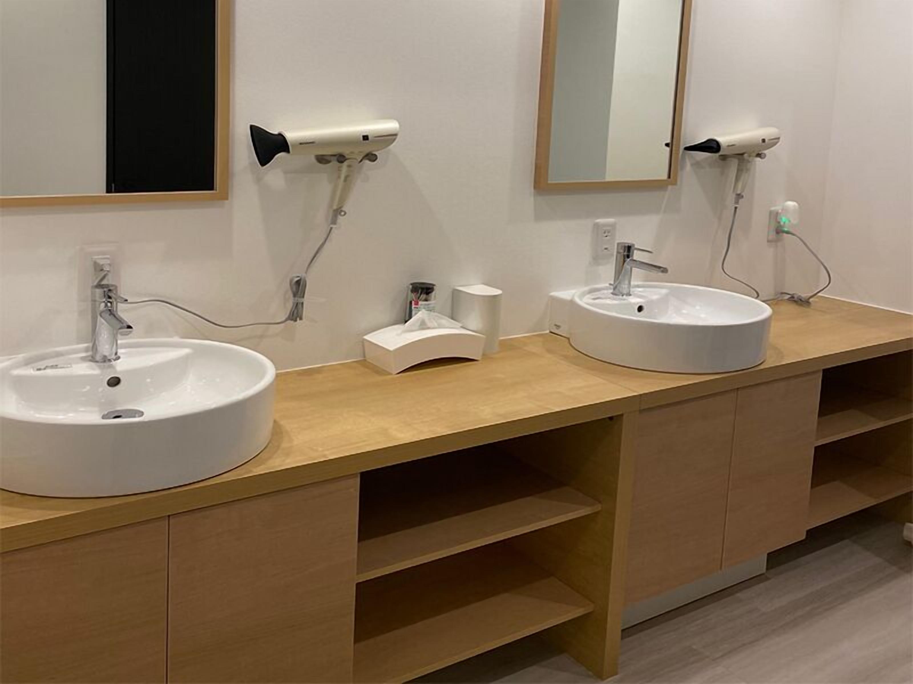 A modern bathroom with two sinks, a mirror, and a hairdryer mounted on the wall.