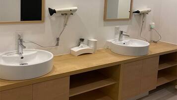A modern bathroom with two sinks, a mirror, and a hairdryer mounted on the wall.