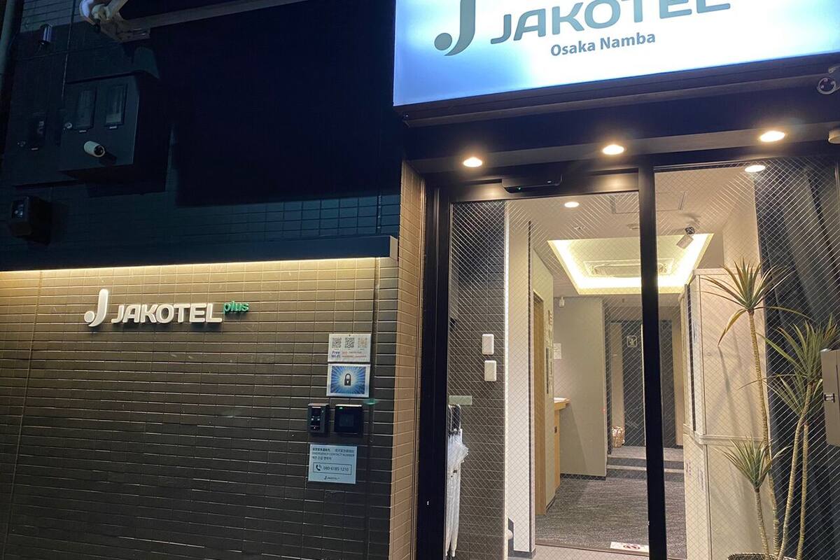 The exterior of a JAKOTEL Plus hotel with a modern design, featuring a prominent entrance and a signboard.