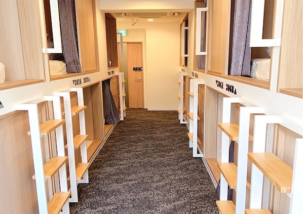 A corridor with bunk beds and storage shelves, leading to a door at the end. - JAKOTEL Plus Namba (Osaka)