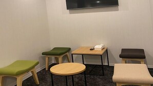 A small, private room with a flat-screen TV mounted on the wall, a small round table, and three chairs with cushioned seats. - JAKOTEL Plus Namba (Osaka)