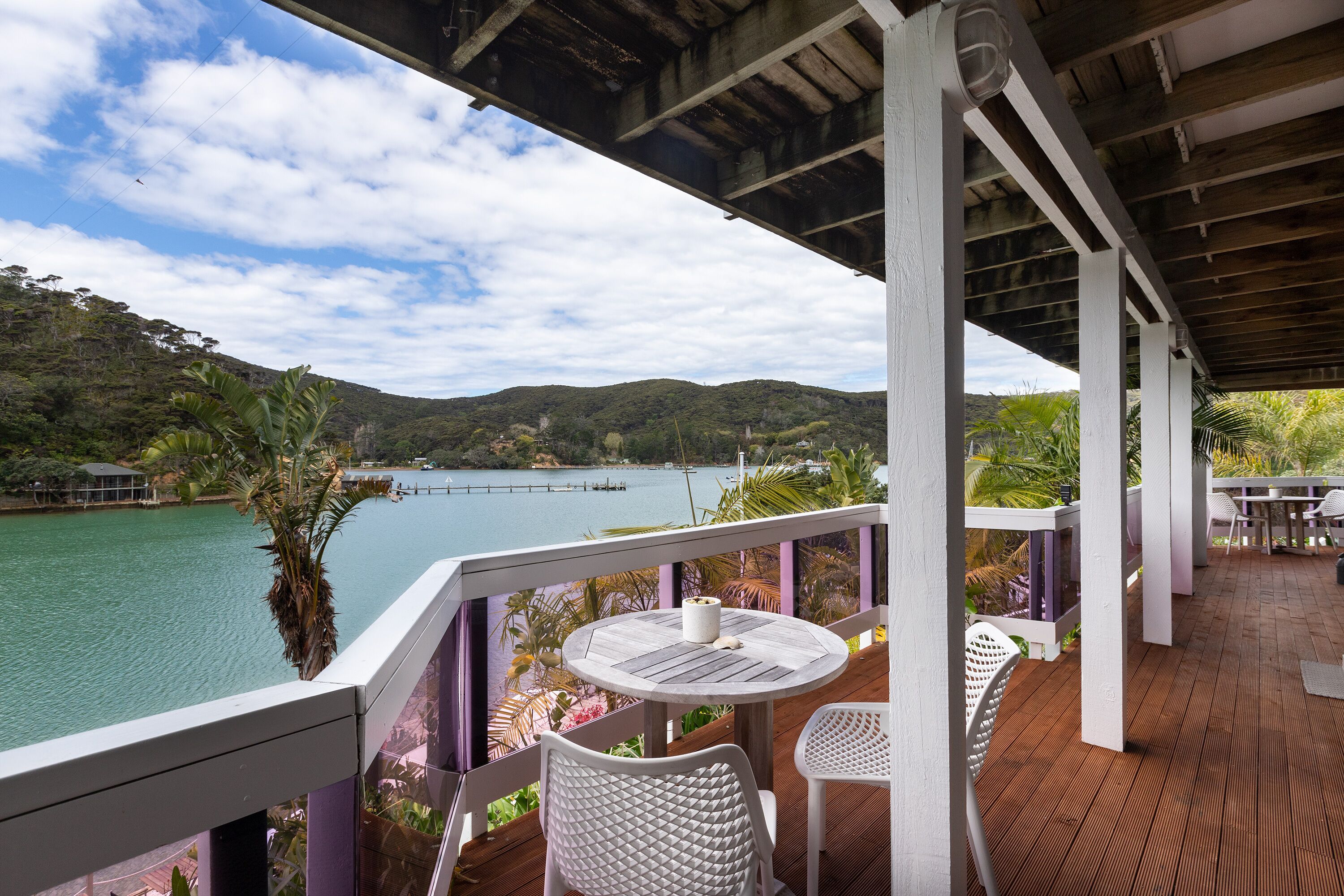 A wooden deck with a table and chairs overlooking a body of water and hills.