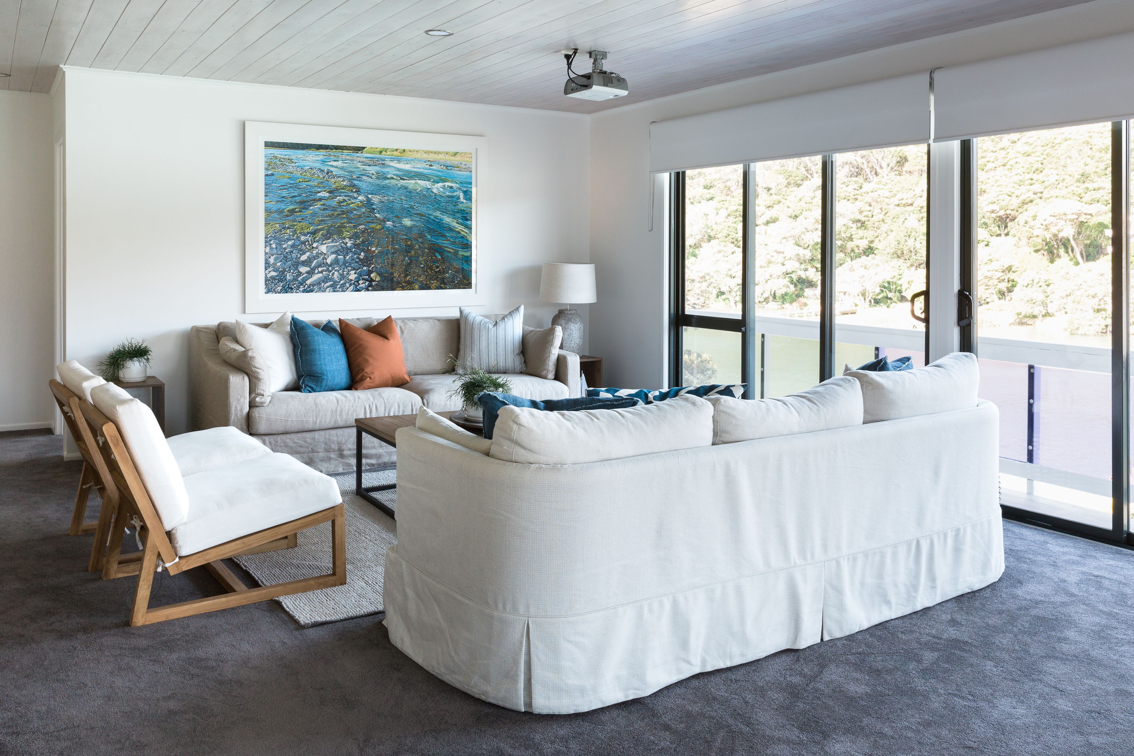 A modern living room with a white sofa, a wooden chair, and a large window offering a view of the outdoors.
