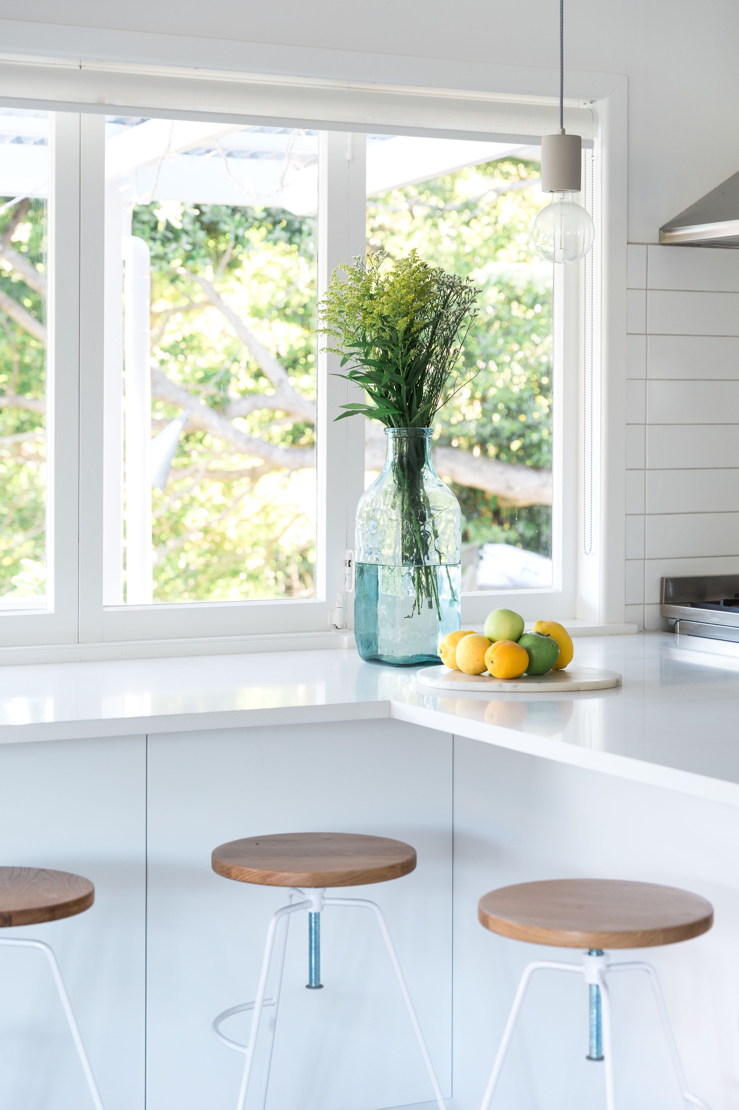 A kitchen with a white countertop, a vase with greenery, and a fruit bowl.