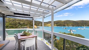 A balcony with a table and chairs, overlooking a bay with boats and greenery.