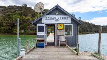 A wooden pier leading to a lodge with a sign reading "Kawau Lodge Events Retreat North Cove."