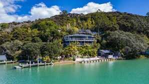 A coastal hotel with a large building surrounded by lush greenery and a clear blue sky. - Kawau Lodge Boutique Resort (Kawau Island)