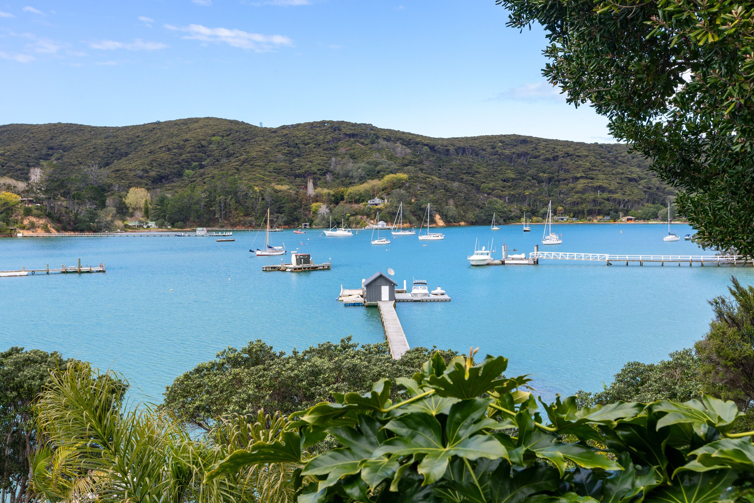 Una marina costera con barcos amarrados, un muelle y colinas al fondo.