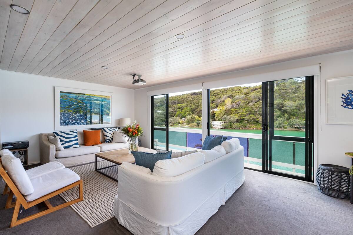 A spacious living area with a white sofa, a coffee table, and a view of a lake through large windows.