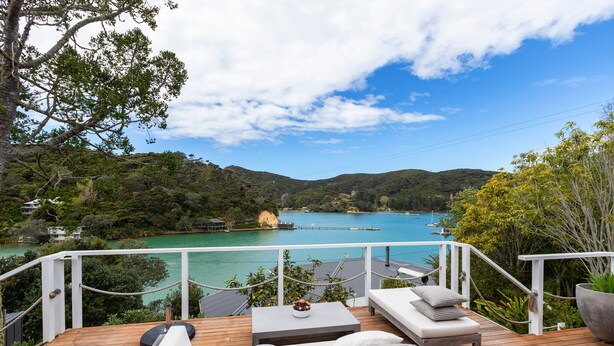 A wooden deck with outdoor seating, overlooking a body of water and hills. - Kawau Lodge Boutique Resort (Kawau Island)