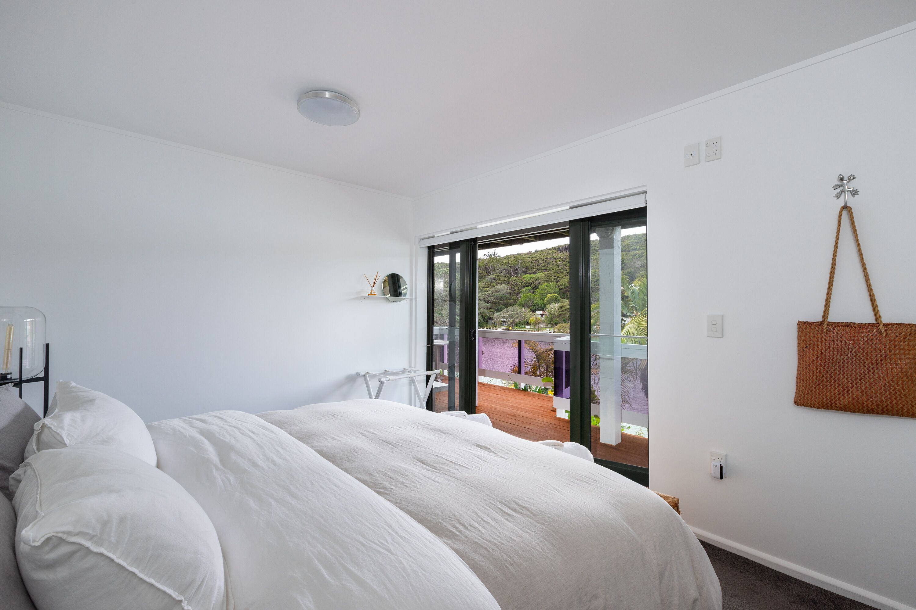 A bedroom with a large bed, a view of a balcony, and a hanging basket.