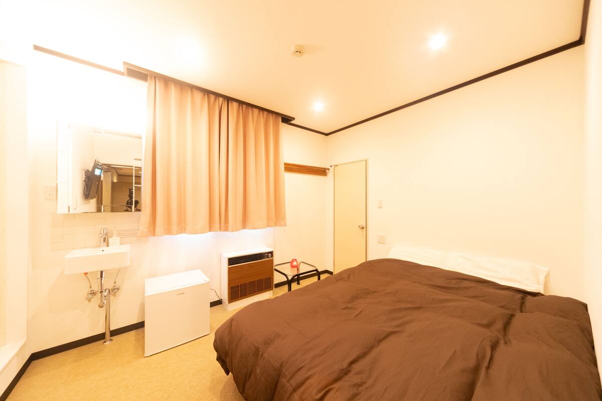 Habitación de hotel con cama, un escritorio pequeño, un espejo, un lavamanos y una puerta.