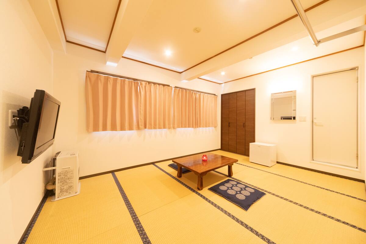 Una habitación con suelo de tatami, una mesa de madera, un televisor y una puerta corredera.