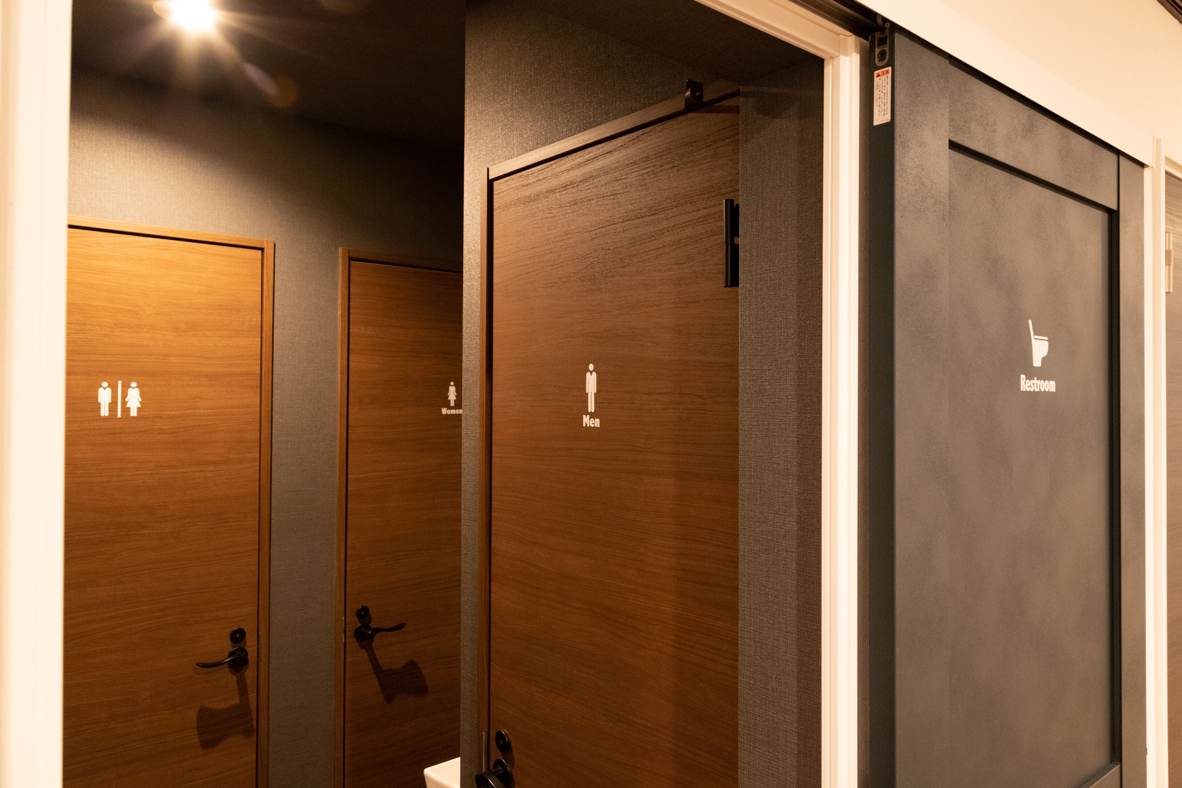 A row of wooden and black restroom doors with gender-specific signage.
