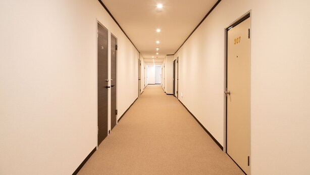 Un pasillo largo y estrecho con puertas a ambos lados, que conduce a una habitación luminosa al final.