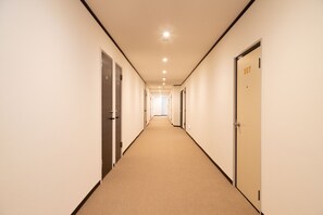 Un pasillo largo y estrecho con puertas a ambos lados, que conduce a una habitación luminosa al final.