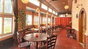 Un restaurante con varias mesas y sillas, ventanas amplias y lámparas colgantes.