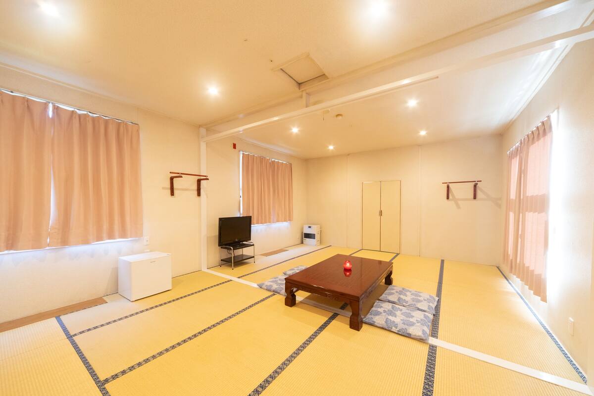 Una habitación con suelo de tatami, una mesa de madera, un televisor y un armario.