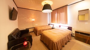 Habitación de hotel con dos camas, un escritorio, una silla, un televisor, una lámpara y una ventana con cortinas.