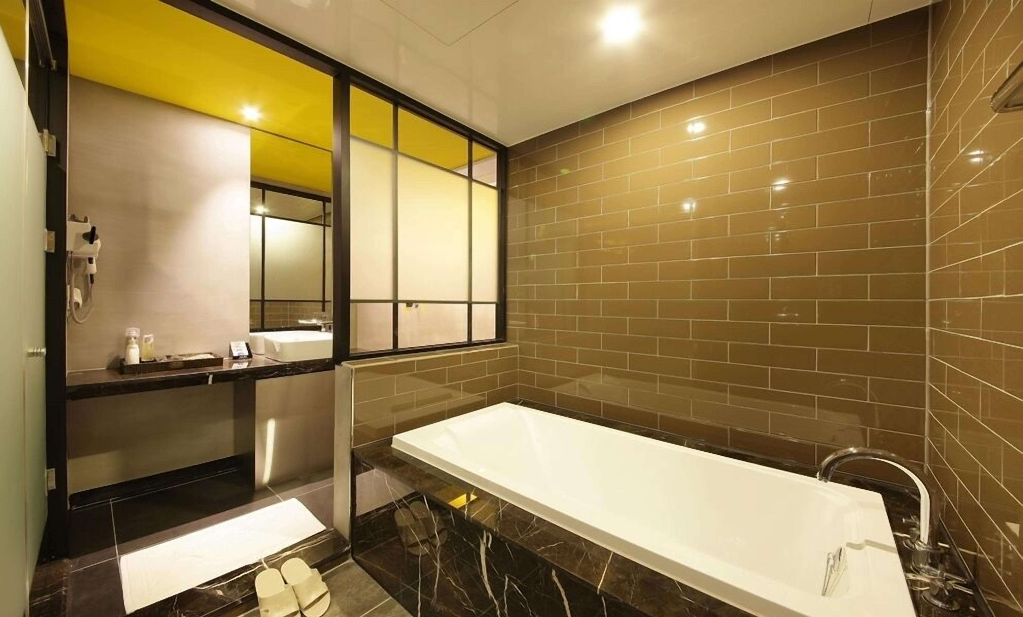 Un baño moderno con una bañera grande, un espejo y una ventana con vidrio teñido de amarillo.