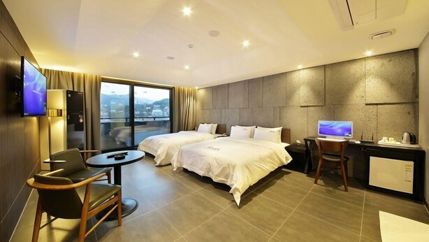 Een hotelkamer met twee bedden, een bureau, een stoel, een televisie en uitzicht op de stad.