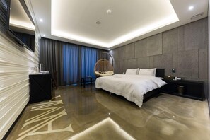 Une chambre moderne avec un grand lit, un fauteuil suspendu, une table de chevet et un banc intégré.