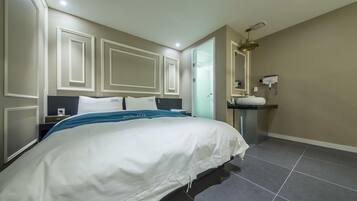 A hotel room with a large bed, a bedside table, a mirror, a sink, and a door leading to another room.