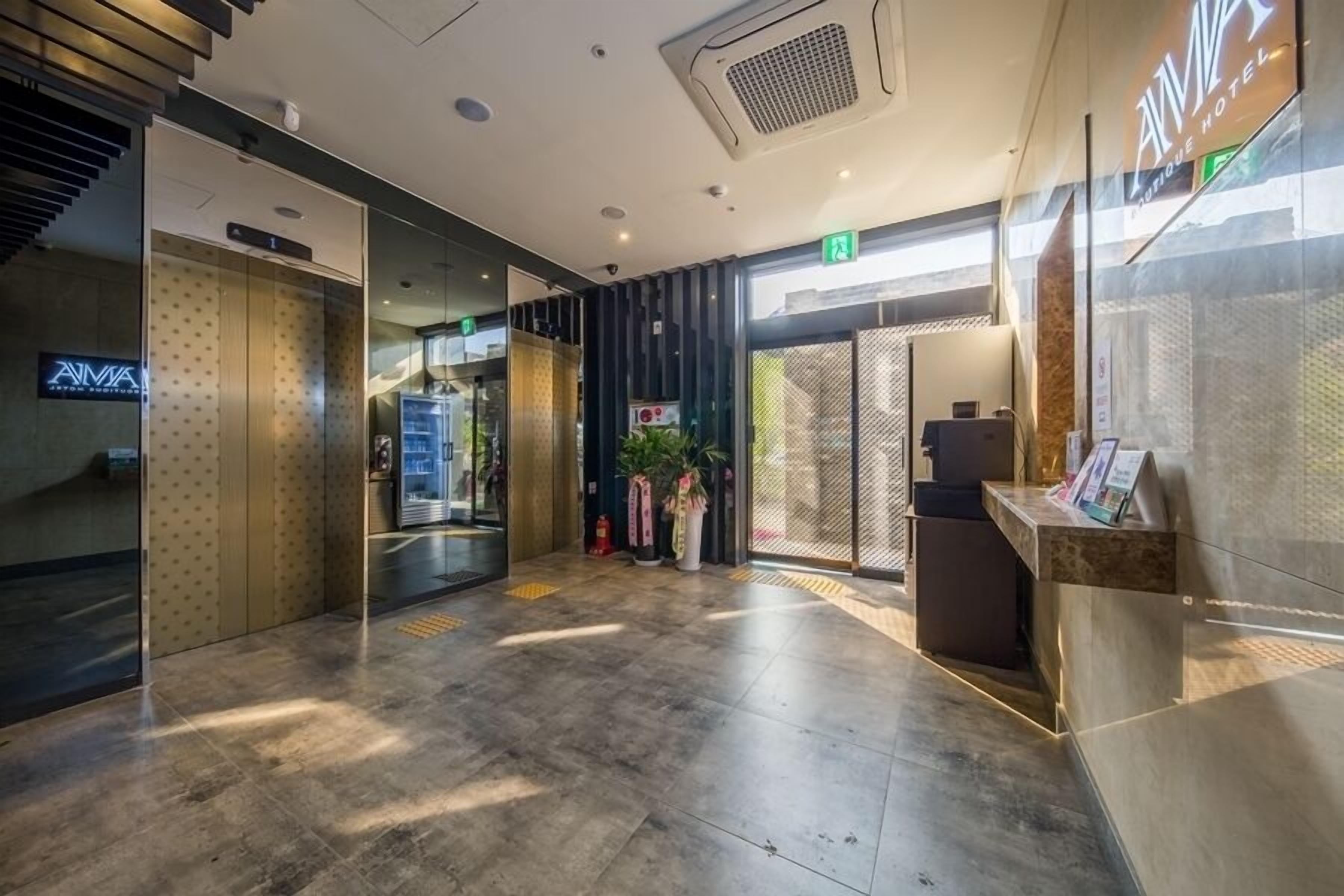 A modern hotel lobby with a reception desk, a staircase, and an elevator.
