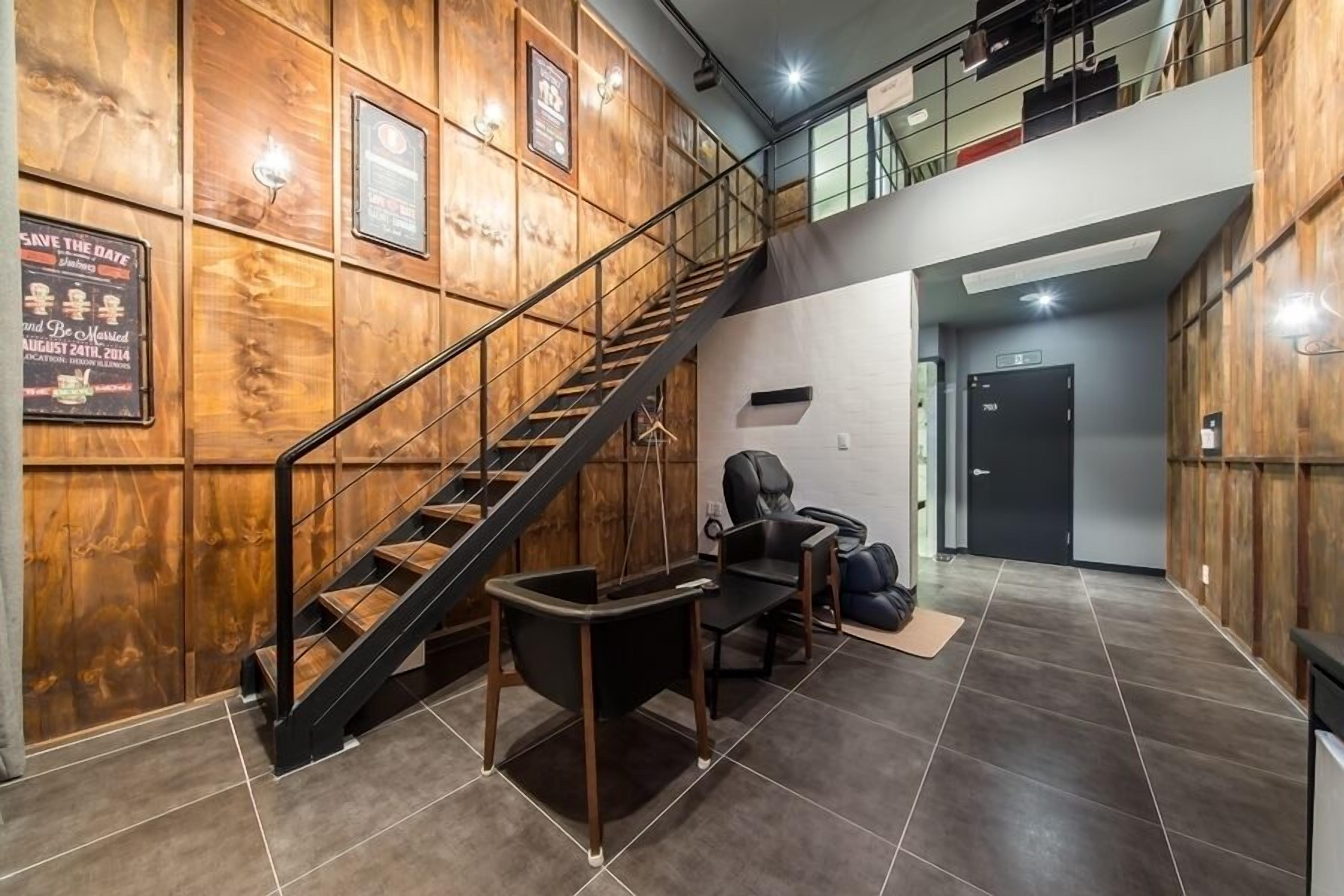 A hotel lobby with a wooden wall, a staircase, a reception desk, and a black leather chair.